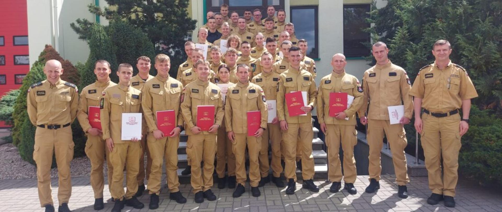 Na zdjęciu widać absolwentów 4 kursu w 2026 roku, stoją oni przed budynkiem i trzymają w rękach dyplomy ukończenia szkolenia