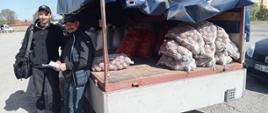 dwóch mężczyzn stoi przed skrzynią ładunkowa samochodu z workami ziemniaków