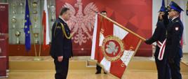 Łódzki Komendant Wojewódzki Państwowej Straży Pożarnej stoi przed sztandarem Komendy Wojewódzkiej PSP w Łodzi oddając mu honor