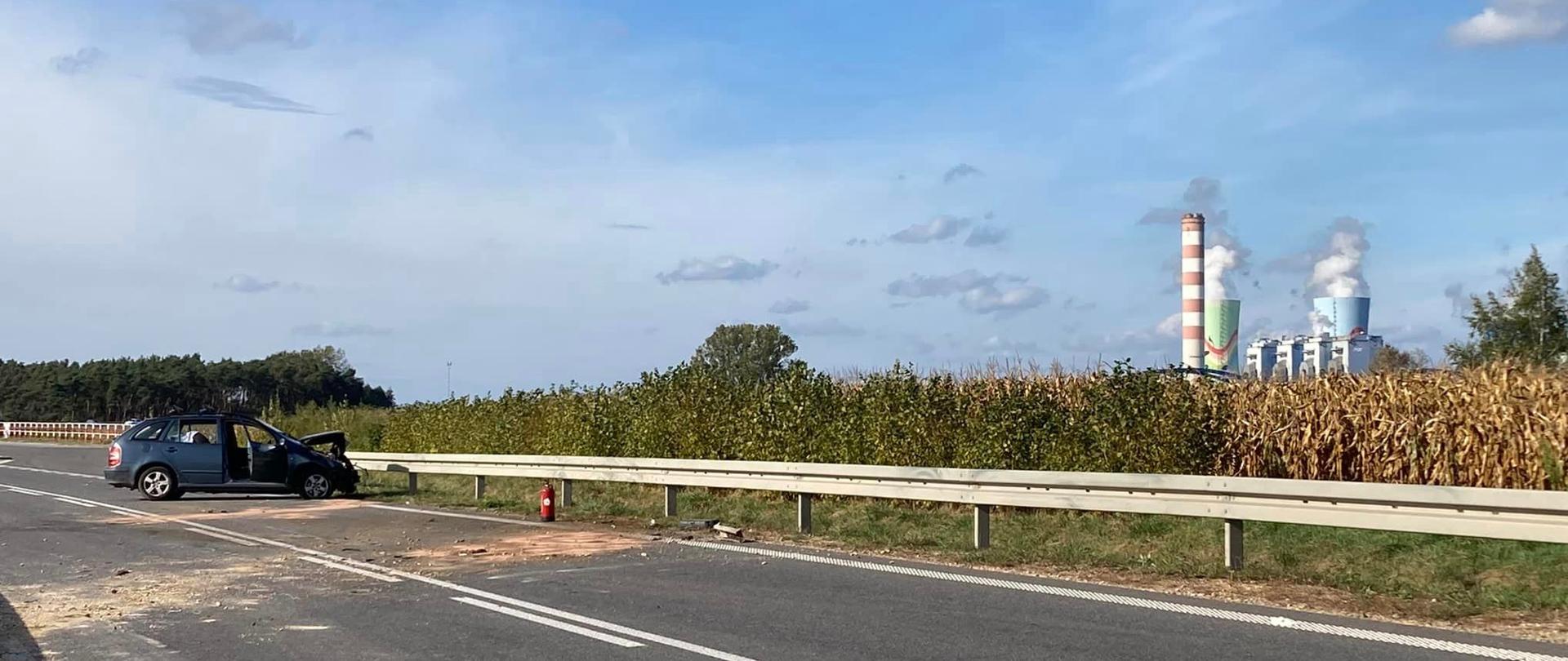 Na zdjęciu widać wrak samochodu osobowego, który stoi przy barierze energochłonnej. W tle widać pole kukurydzy i kominy