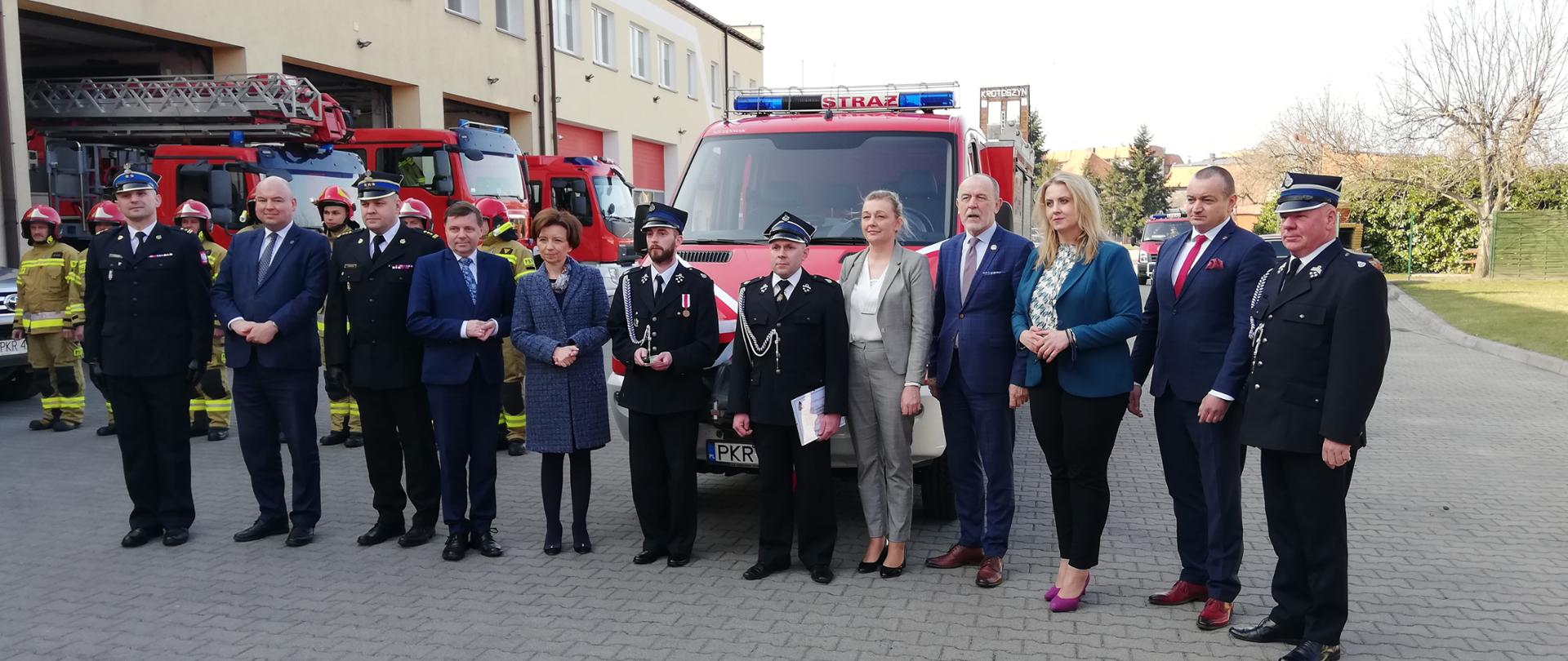 Zdjęcie przedstawia pozujących do wspólnego zdjęcia zaproszonych gości na tle przekazywanego pojazdu.