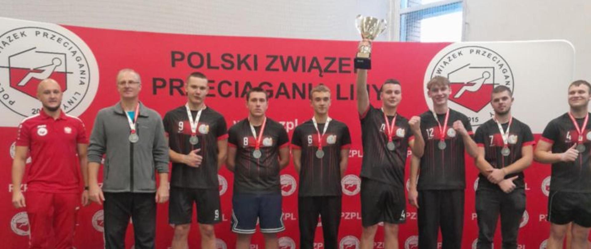 Uczniowie z nauczycielami na podium trzymają puchar.