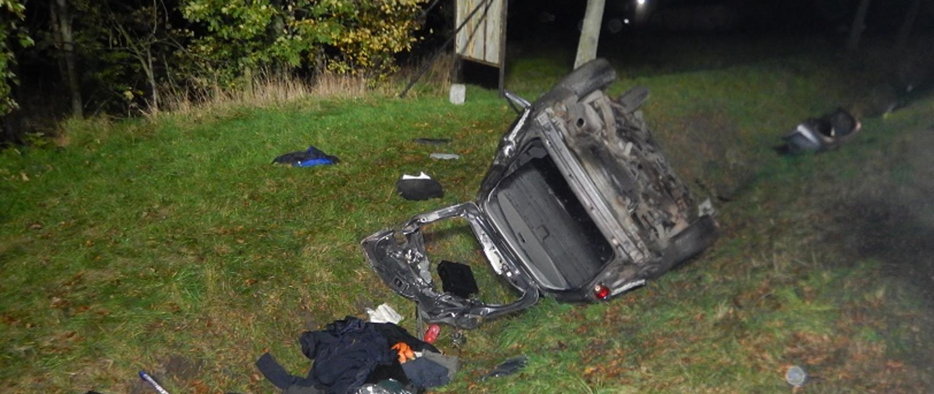 Zdjęcie przedstawia uszkodzony samochód w wyniku wypadku drogowego, leżący na dachu w przydrożnym rowie. Do wypadku doszło w porze nocnej.