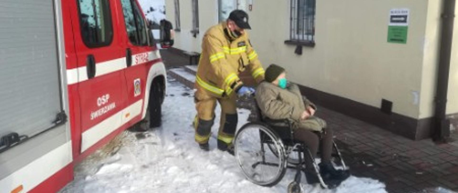 Na zdjęciu strażak pcha wózek z niepełnosprawną