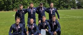 Zdjęcie przedstawia drużynę brodnickiej komendy, która zajęła drugie miejsce na czwartych Kujawsko-Pomorskie Zawodach Pożarniczego Ćwiczenia Bojowego. Strażacy pozują na murawie boiska w granatowych dresach. Stoją w dwóch rzędach - pierwsza czwórka kuca a za nimi stoi druga czwórka. Na szyjach sportowców wiszą medale. W dolnym rzędzie strażacy trzymają w dłoniach czek będący nagrodą. Drugi strażak trzyma puchar, a trzeci pamiątkowy dyplom.