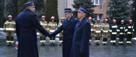 W tle zbiórka strażaków w umundurowania bojowym. Na pierwszym planie strażacy w umundurowaniu galowym , w płaszczach zimowych. Komendant powiatowy PSP wręcza akt mianowania dla mł.bryg. Dozda