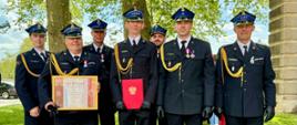 Funkcjonariusze Komendy Powiatowej Państwowej Straży Pożarnej w Krośnie Odrzańskim w mundurach wyjściowych po otrzymaniu awansów oraz odznaczeń po Wojewódzkich Obchodach Dnia Strażaka. Dwóch strażaków trzyma dyplom i czerwoną teczkę.