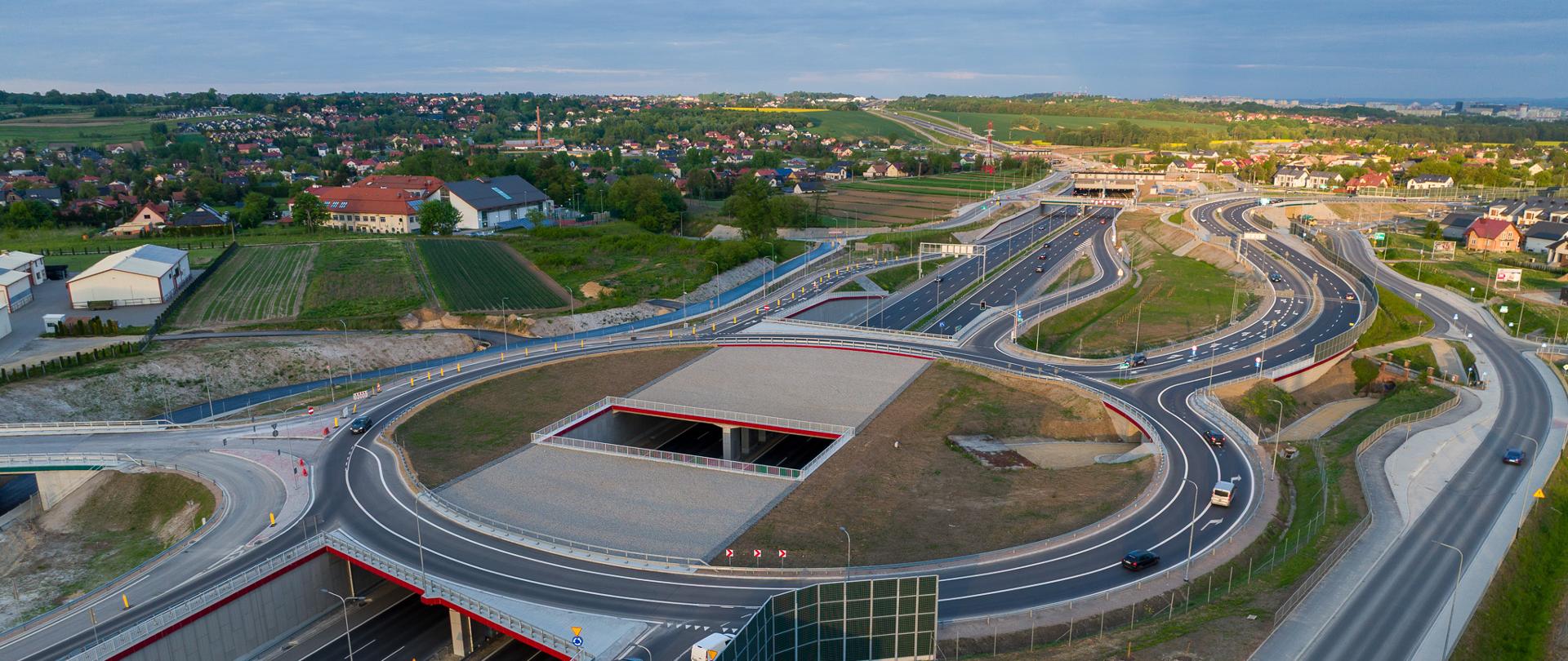 S52 Północna Obwodnica Krakowa, węzeł Zielonki i tunel, po obu stronach drogi zabudowania, w oddali pola, zadrzewienia i krakowskie osiedla
