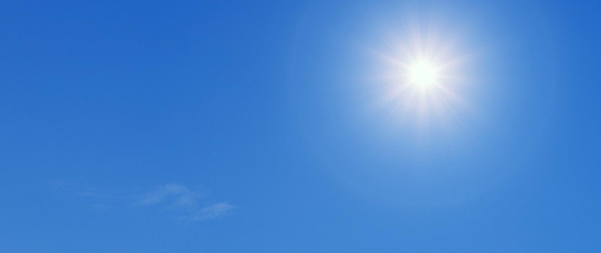 Jasne niebo z promieniami słońca w prawym górnym rogu i lekkimi chmurami w lewym dolnym rogu.