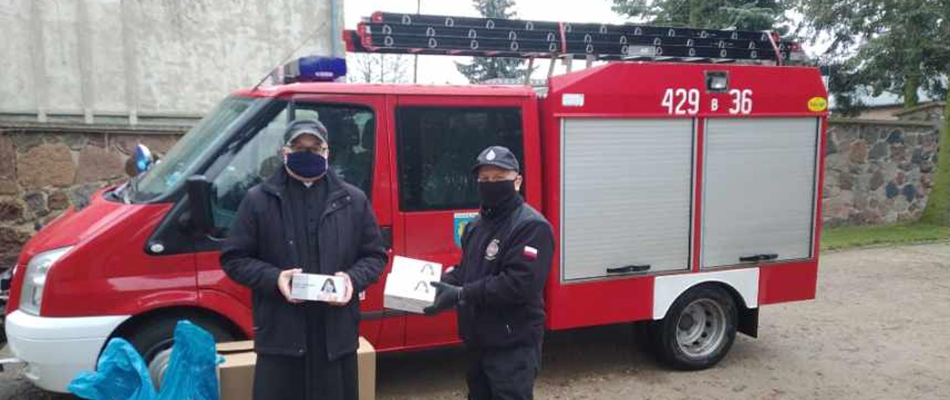 Strażak OSP oraz ksiądz. W tle samochód pożarniczy.