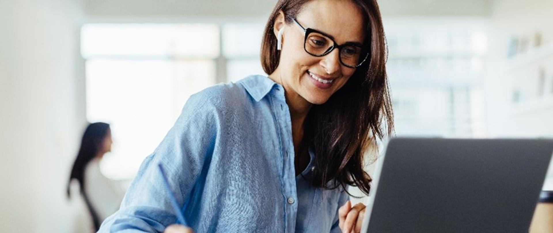 Kobieta siedzi przed laptopem i notuje