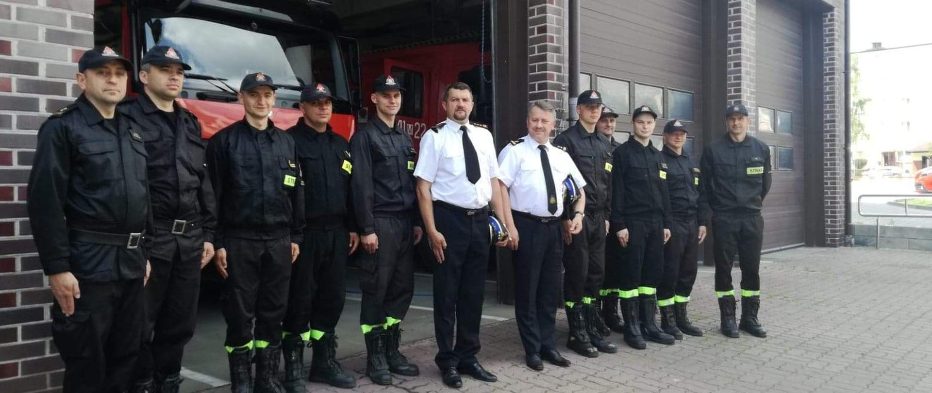 Wizyta Mazowieckiego Komendanta Wojewódzkiego. Strażacy stojący w szeregu na tle strażnicy.