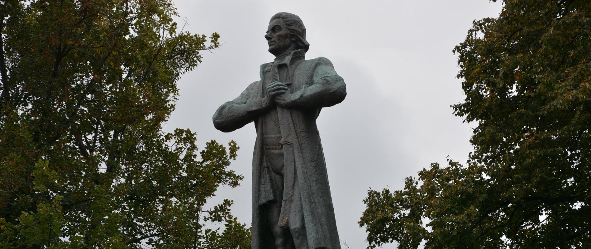 na tle drzew widoczny kamienny pomnik przedstawiający mężczyznę 