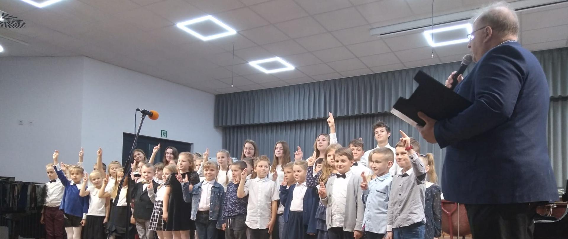 Dyrektor Szkoły pan Andrzej Jórkowski oraz uczniowie klas pierwszych działu dziecięcego i młodzieżowego na scenie podczas ślubowania