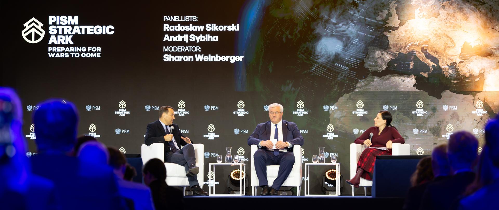 Na zdjęciu są trzy osoby - dwóch mężczyzn i kobieta. Siedzą na scenie na białych fotelach. Mówią do mikrofonów. Za nimi w tle napis "PISM Strategic Ark"