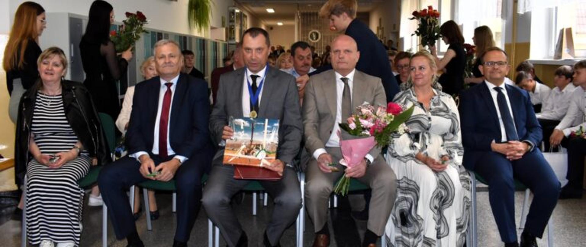 Nauczyciele siedzą w pierwszym rzędzie podczas uroczystości szkolnej.