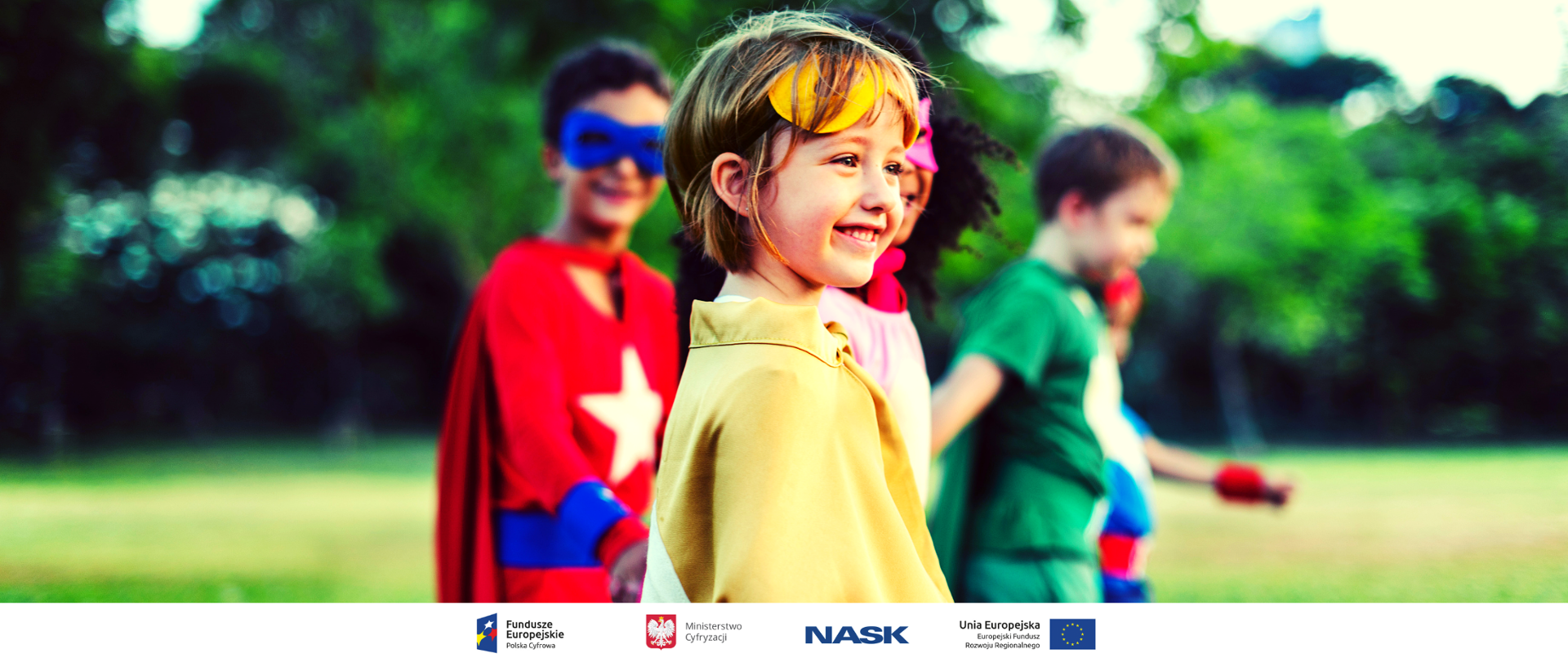 Na zdjęciu widać grupę uśmiechniętych dzieci w strojach superbohaterów, przebywających w otoczeniu drzew. U dołu znajduje się pasek logotypów: Europejskie Fundusze Polska Cyfrowa, Ministerstwo Cyfryzacji, NASK i Unia Europejska Europejski Fundusz Rozwoju Regionalnego.