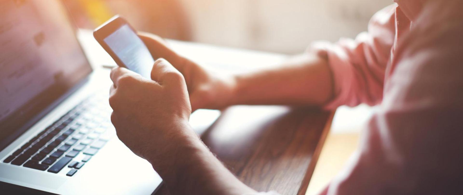 Męskie dłonie, smartfon i laptop