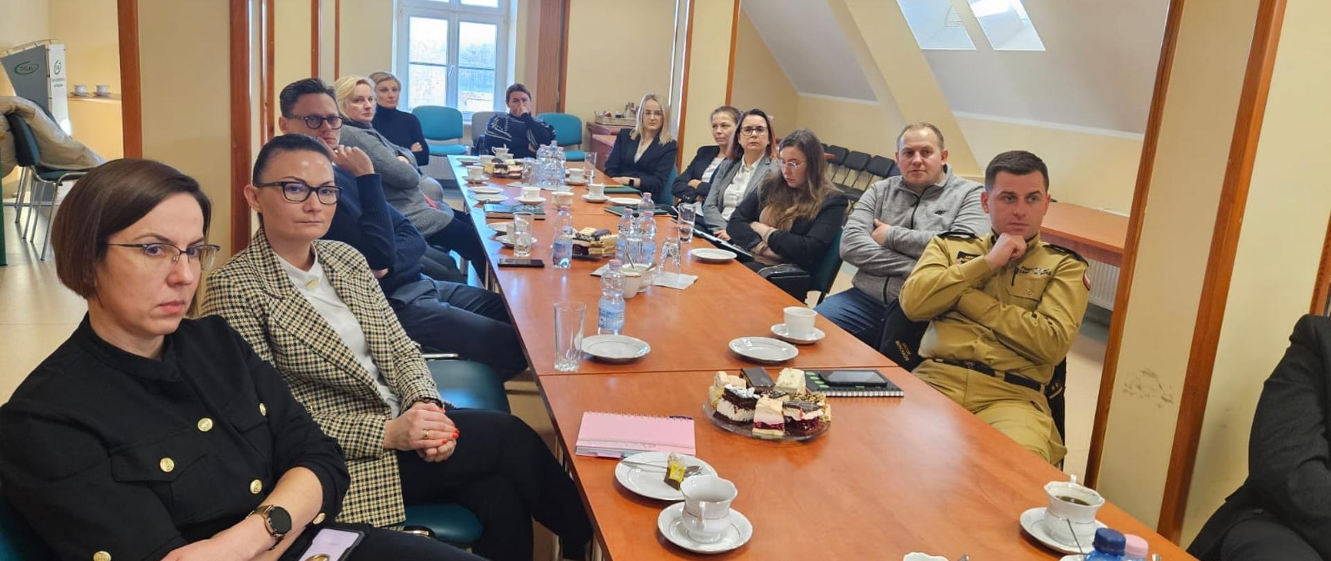 Osoby biorące udział w szkoleniu siedzą przy stole i obserwują ekran