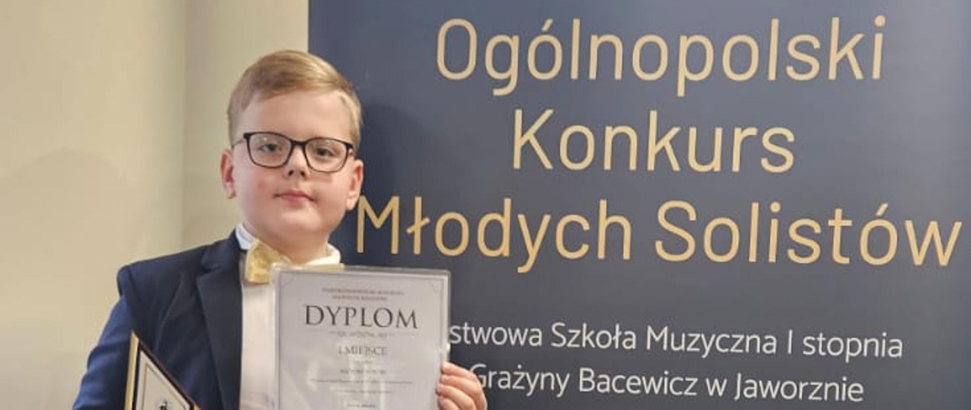 Chłopiec z dyplomem i statuetką na tle baneru konkursu