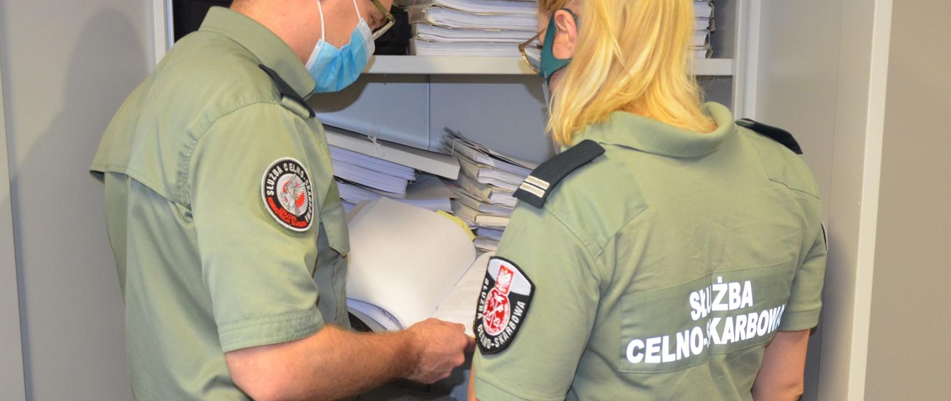 Funkcjonariusz i funkcjonariuszka Służby Celno-Skarbowej podczas przeglądania dokumentów.