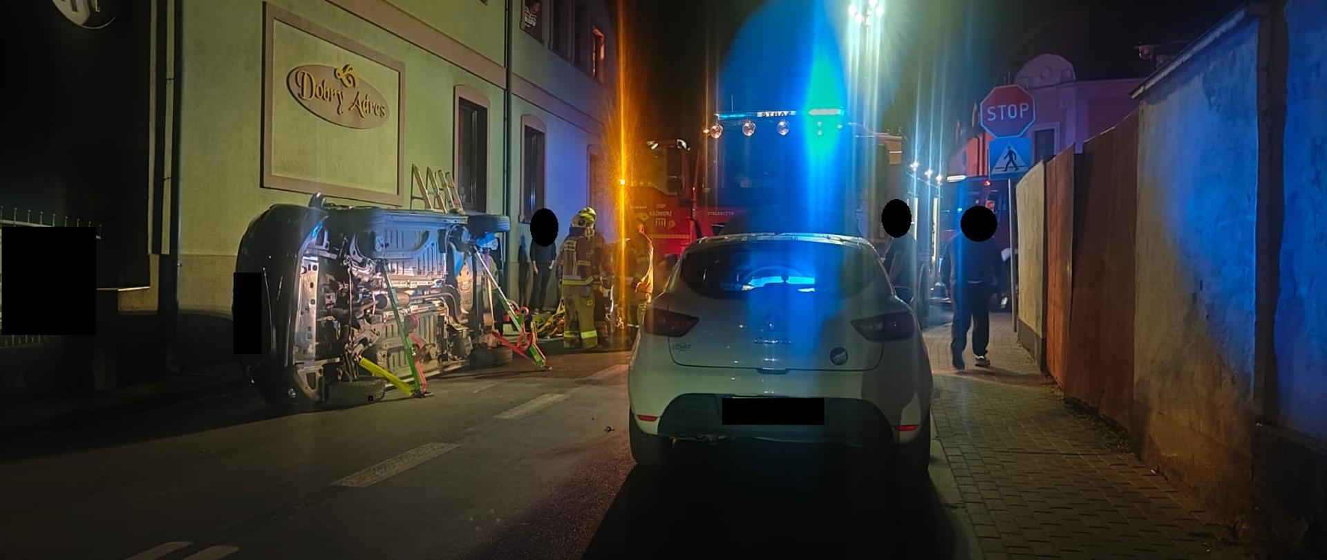 Samochód na prawym boku na drodze, w pobliżu strażacy