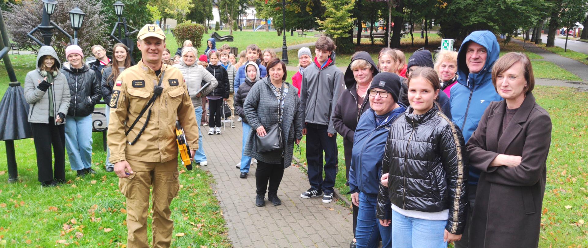uczniowie, nauczyciele i strażak stojący przy punkcie zbornym