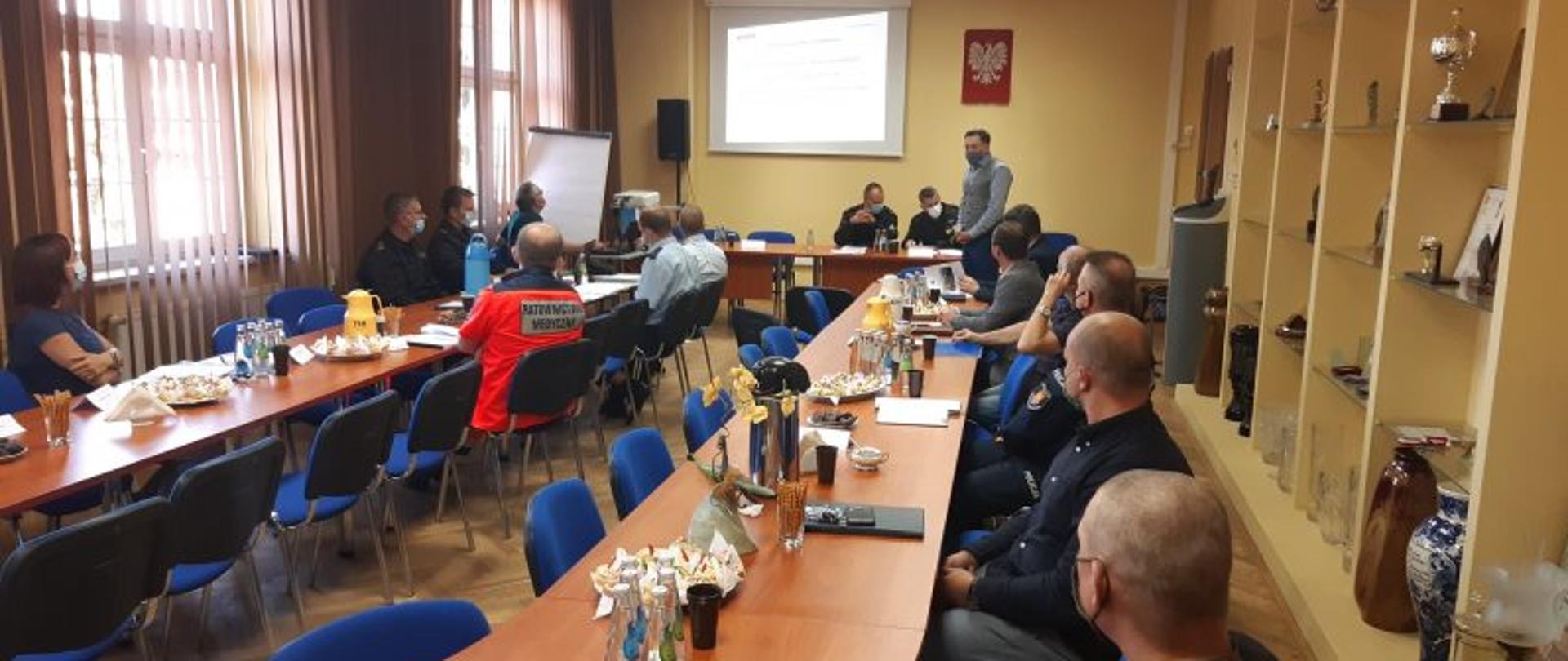 Pomieszczenie we firmie lotos. Duży okrągły stół a dookoła niego siedzą osoby reprezentujące firmę LOTOS oraz władza z KP PSP Jasło