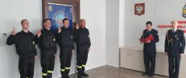 Zdjęcie przedstawia czterech strażaków ubranych w czarne ubrania koszarowe na tle sztandaru Komendy Miejskiej PSP w Świnoujściu składających ślubowanie. Od prawej Komendant Miejski wraz ze swoim Zastępcą.
Wszyscy przebywają w sali konferencyjnej KM PSP w Świnoujściu.