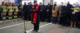 Widok z przodu. Kapelan małopolskich strażaków błogosławi uczestników uroczystości. W tle stoją zaproszeni goście.