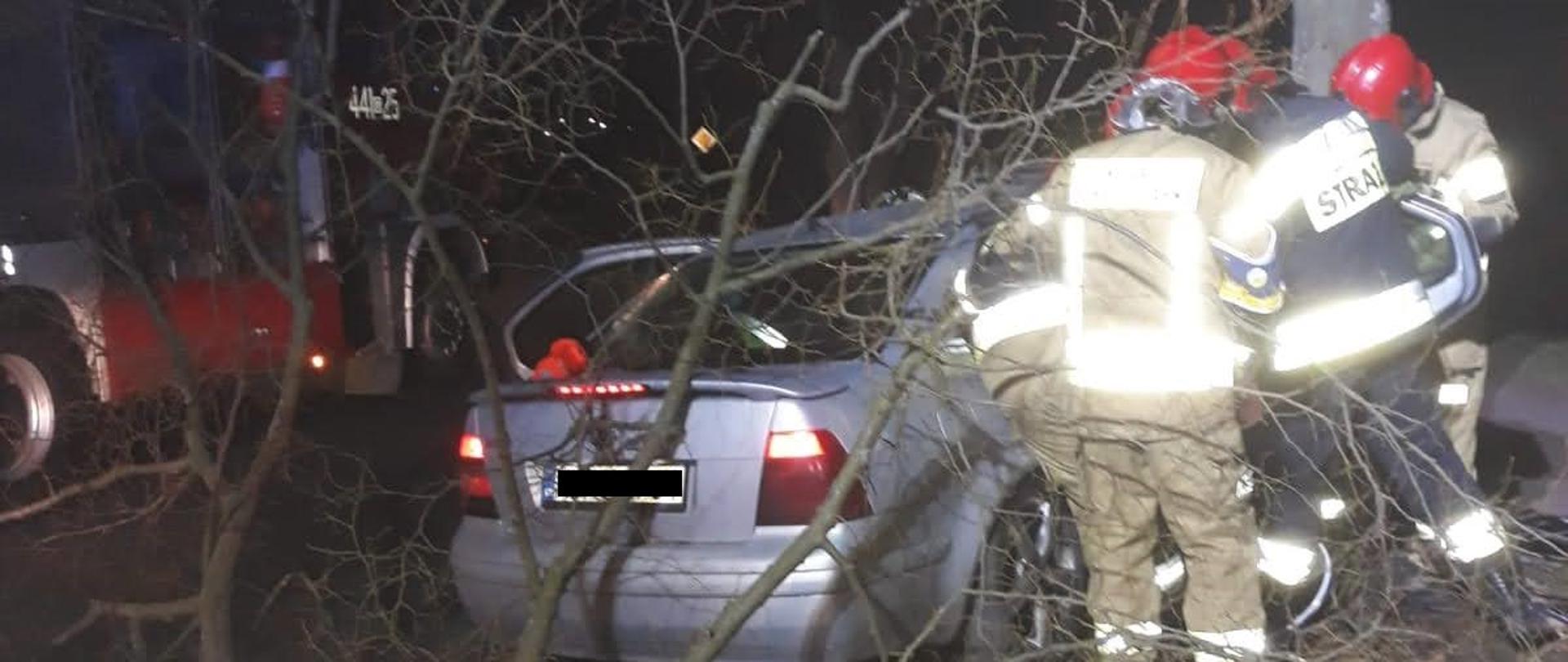 Strażacy w trakcie działań przy uszkodzonym samochodzie
