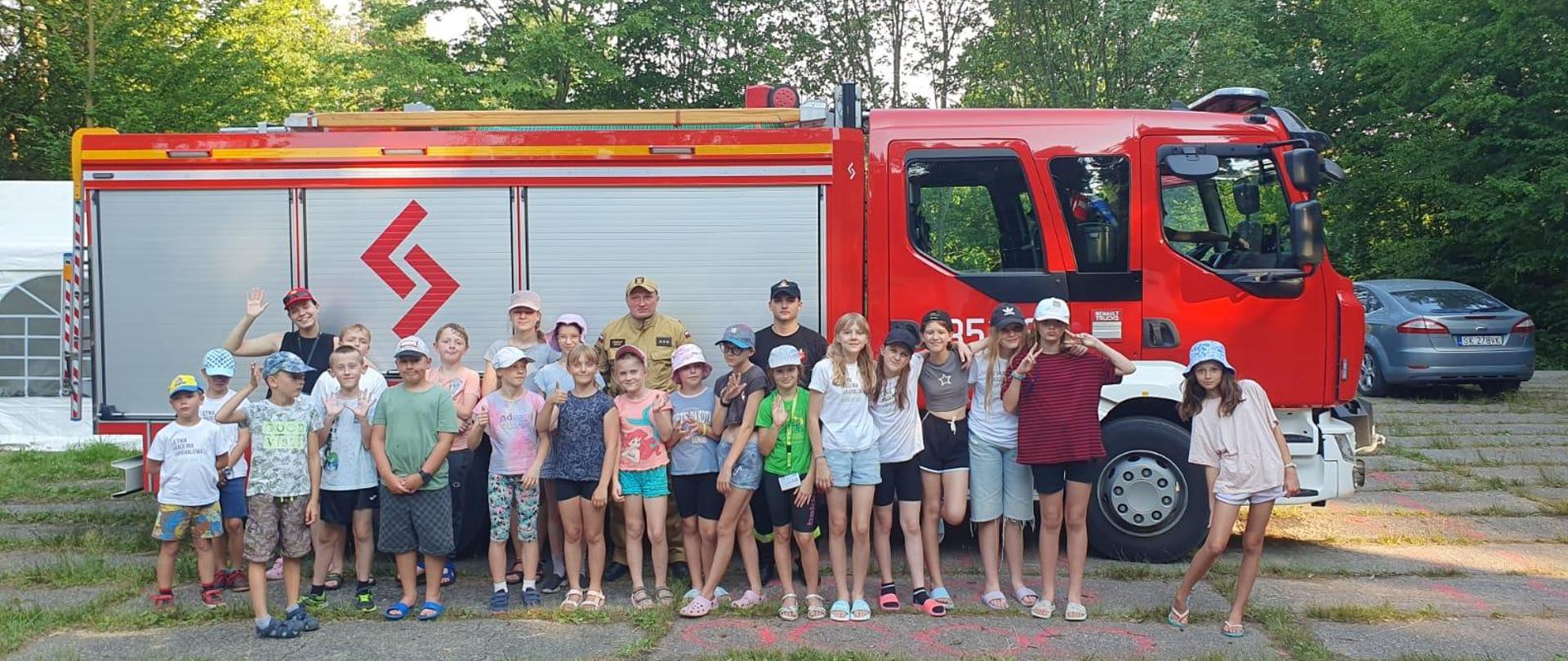 Dzieciaki z ZHP prezentują się na tle wozu strażackiego 