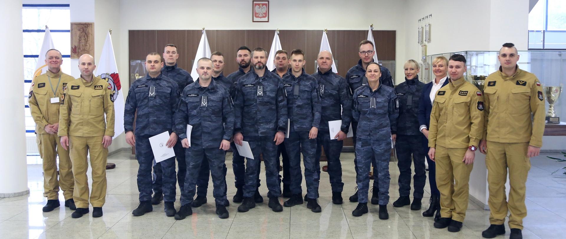 Grupowe zdjęcie uczestników szkolenia (12 osób) w towarzystwie Zastępcy Komendanta Centralnej Szkoły PSP, kobiety oraz trzech strażaków CS PSP