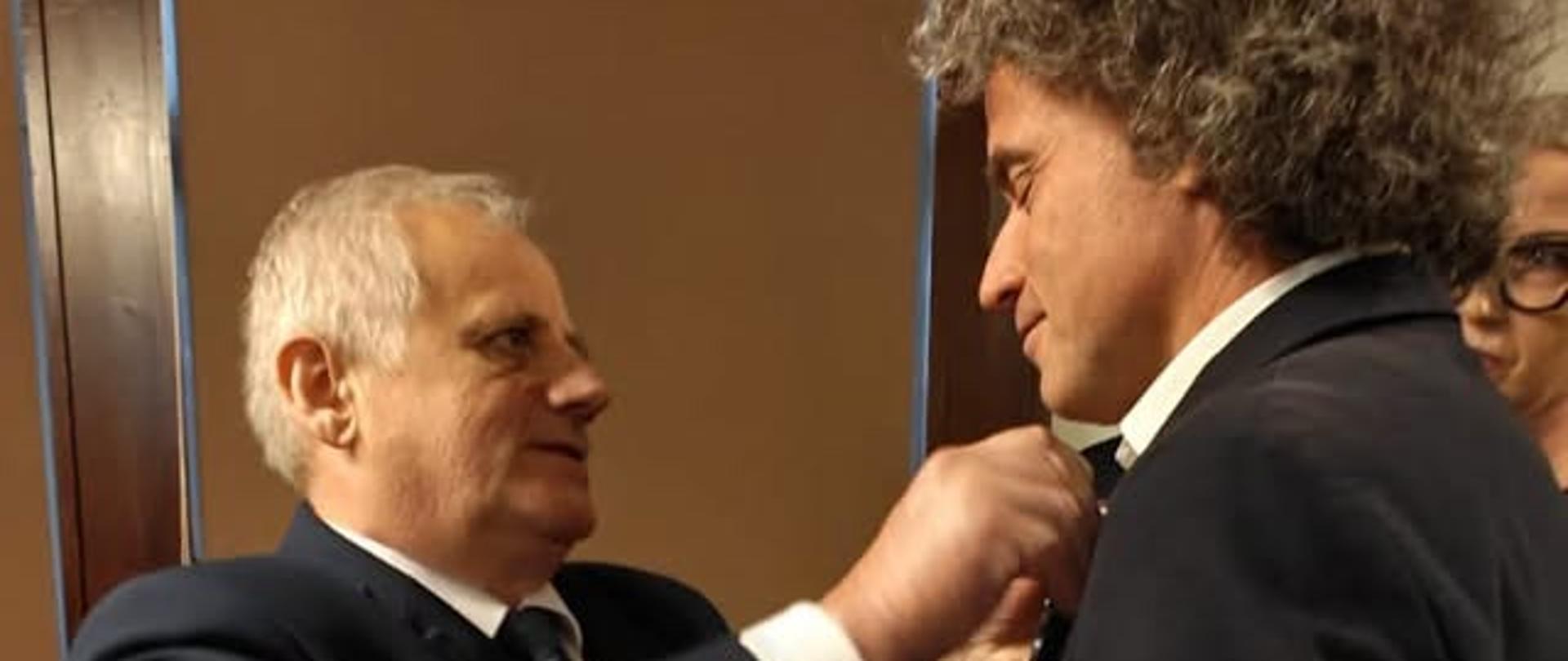 Mężczyzna w garniturze, wicewojewoda, przypina odznaczenie mężczyźnie 