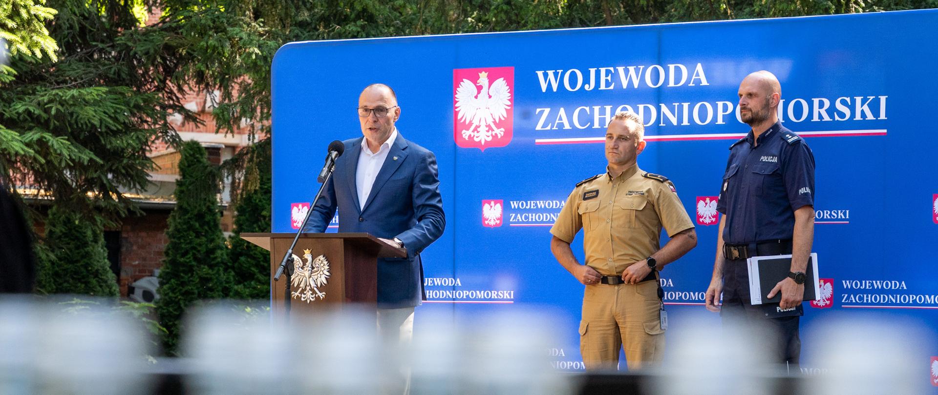 wojewoda przy mównicy, z nim zastępca komendanta policji i rzecznik komendanta psp