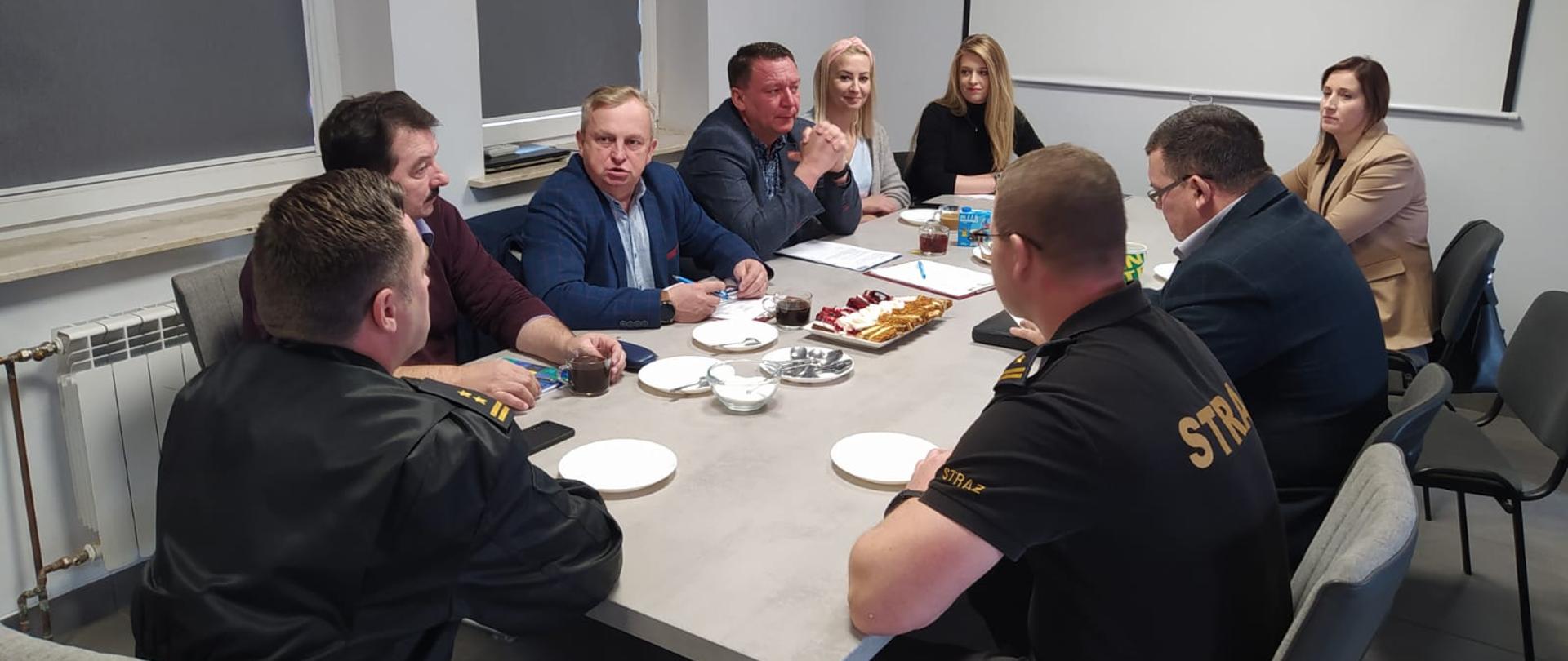 Strażacy wraz z przedstawicielami urzędów gmin siedzą przy stole. 