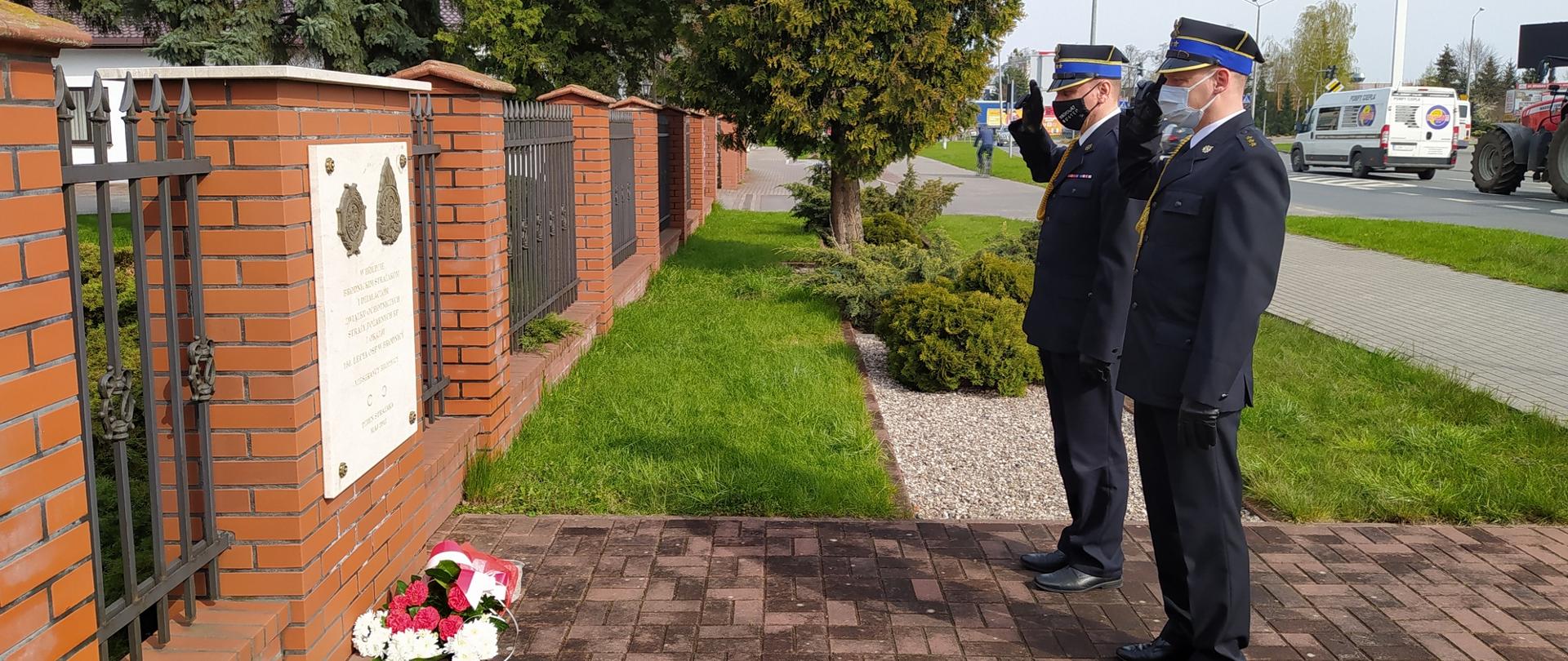 Zdjęcie przedstawia komendantów KP PSP w Brodnicy podczas złożenia wiązanki kwiatów przy tablicy pamiątkowej poświęconej pamięci brodnickich strażaków.