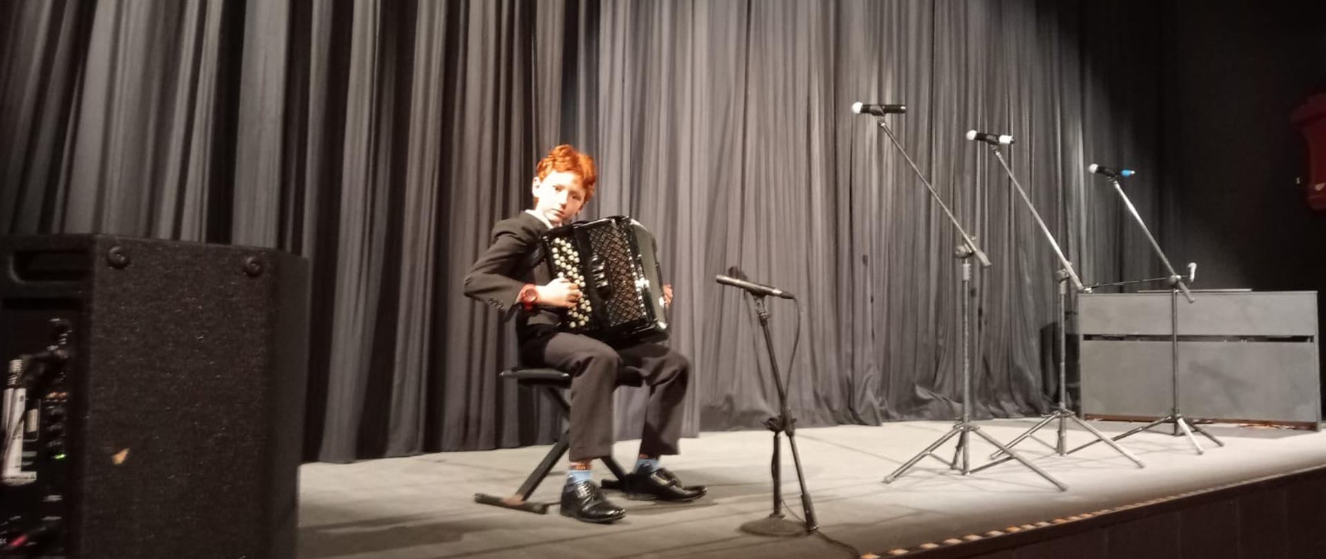 Uczeń Gabriel Charęza siedzi na krześle i gra na akordeonie w Kłodzkim Ośrodku Kultury
