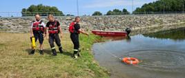 Widoczni policjant i strażacy ściągający do brzegu koło ratownicze.