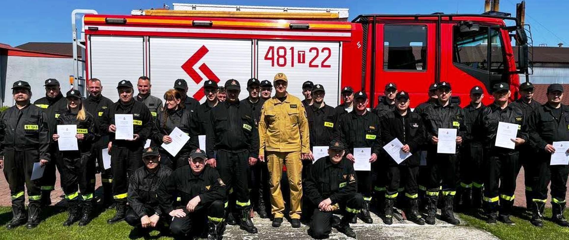 Grupowe zdjęcie osób które ukończyły szkolenie wraz z osobami egzaminującymi na tle samochodu gaśniczego JRG Skarżysko-Kamienna.