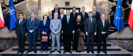 Zdjęcie przedstawia grupę osób ubranych w garnitury. Wśród nich jest minister Radosław Sikorski oraz ambasadorowie państw arabskich akredytowani w Warszawie. Po bokach są flagi Polski, NATO i Unii Europejskiej.