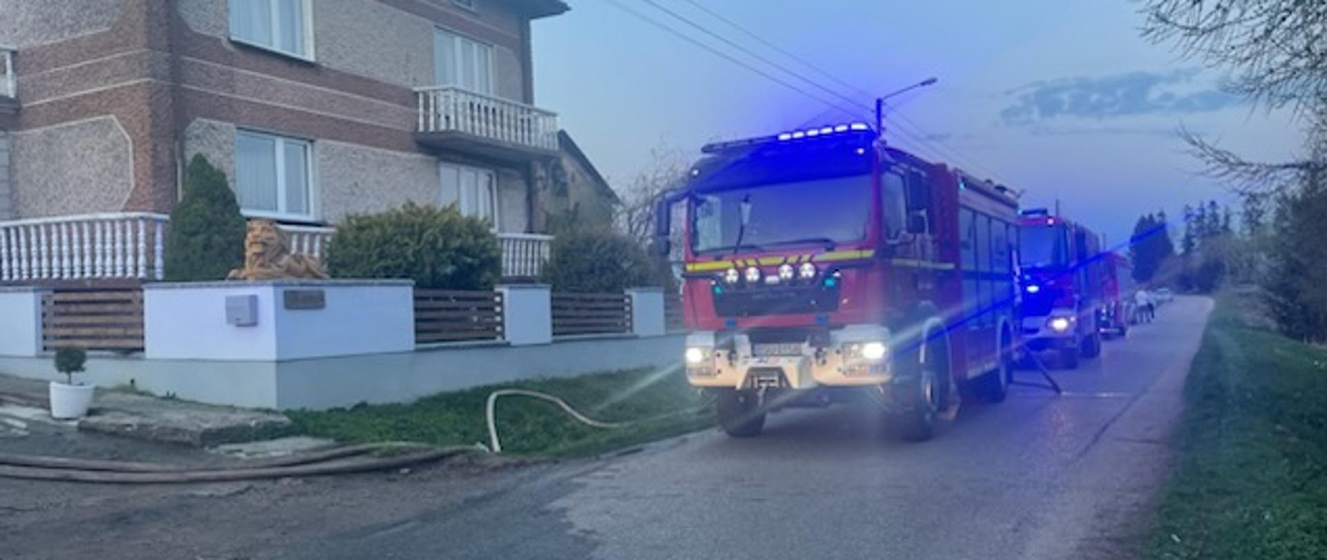 Na ulicy pojazdy pożarnicze przy budynku i linię gaśnicze