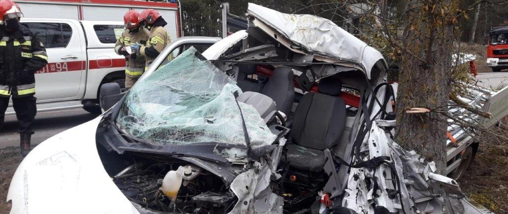 Zniszczony w wypadku samochód dostawczy. W tle strażacy PSP i pojazdy pożarnicze.