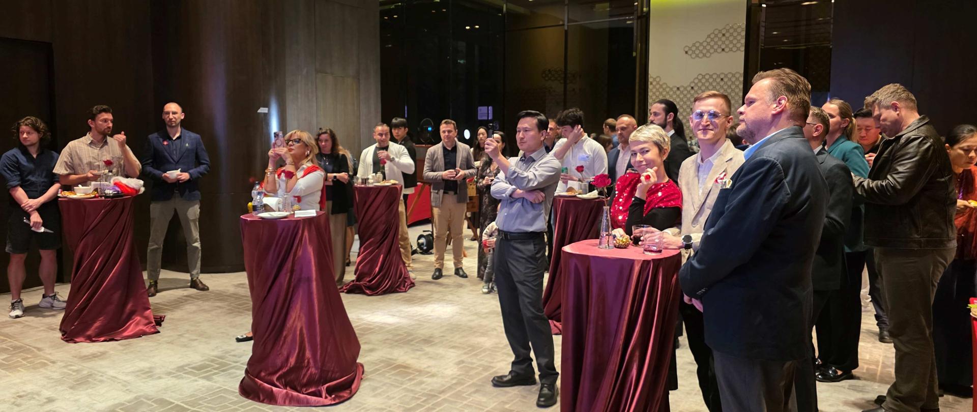 Uczestnicy spotkania bożonarodzeniowego rozmawiają przy stolikach podczas spotkania bożonarodzeniowego.