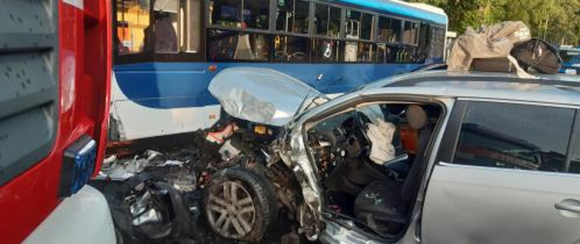 Samochód osobowy uderzył przodem w autobus. Widoczne uszkodzenia karoserii pojazdów. Lewe drzwi pojazdu osobowego usunięte przez Straż Pożarną