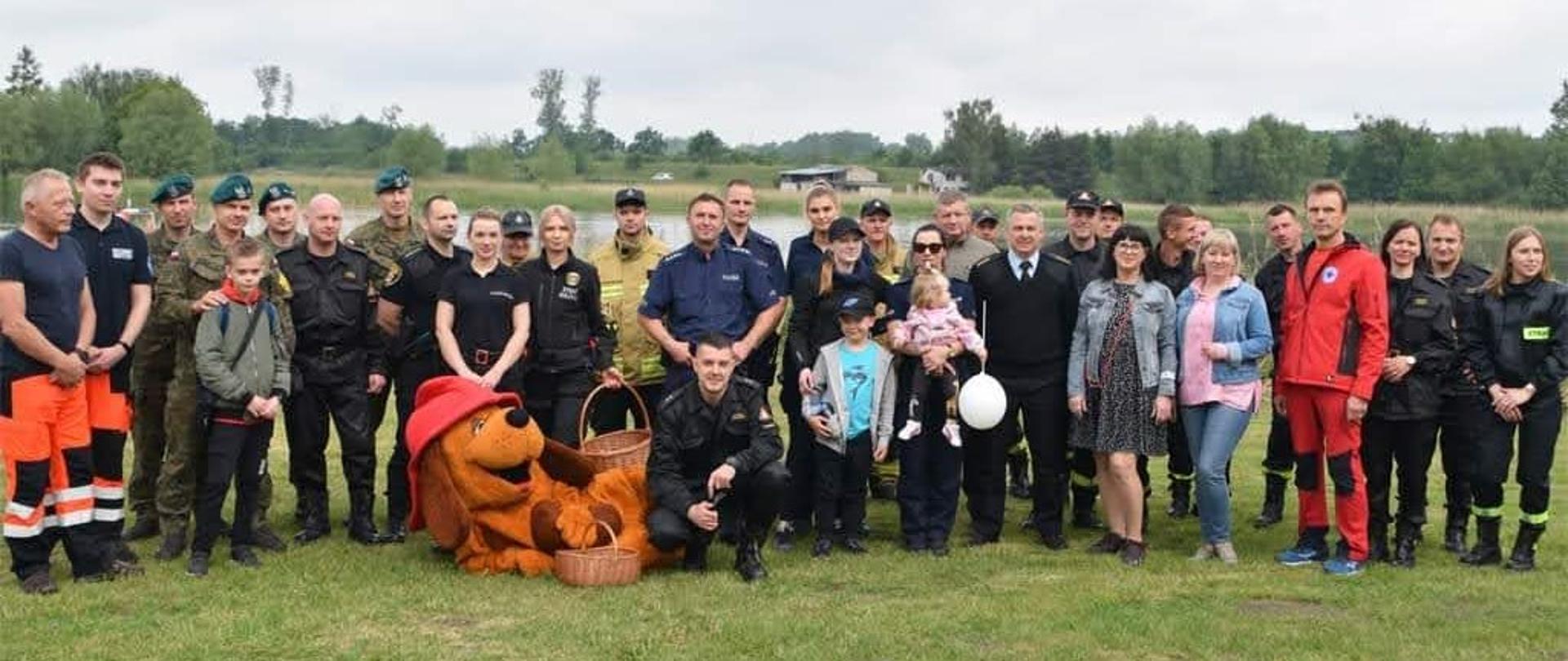 Na zdjęciu znajdują się przedstawiciele instytucji, służb zaangażowanych w organizację Dnia Dziecka, zdjęcie wykonano na tle Jeziora Starogrodzkiego w Chełmnie. 