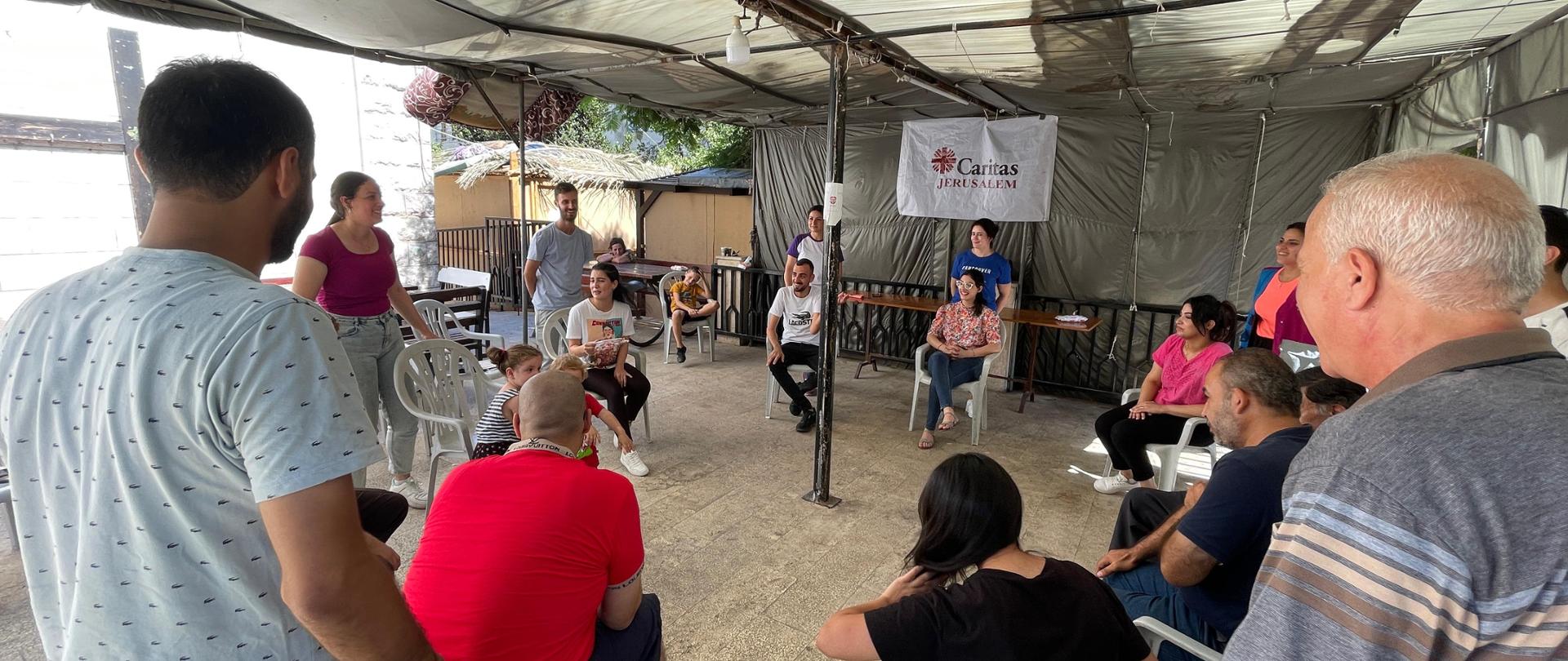 Grupa osób (kobiet i mężczyzn) siedzi na krzesłach ustawionych w koło, rozmawiają