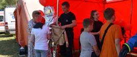 Na zdjęciu widać czerwony namiot wystawowy KM PSP Kalisz. Na zdjęciu funkcjonariusze i sprzęt, który był opisywany dzieciom. Zdjęcie zrobione w ciągu dnia.