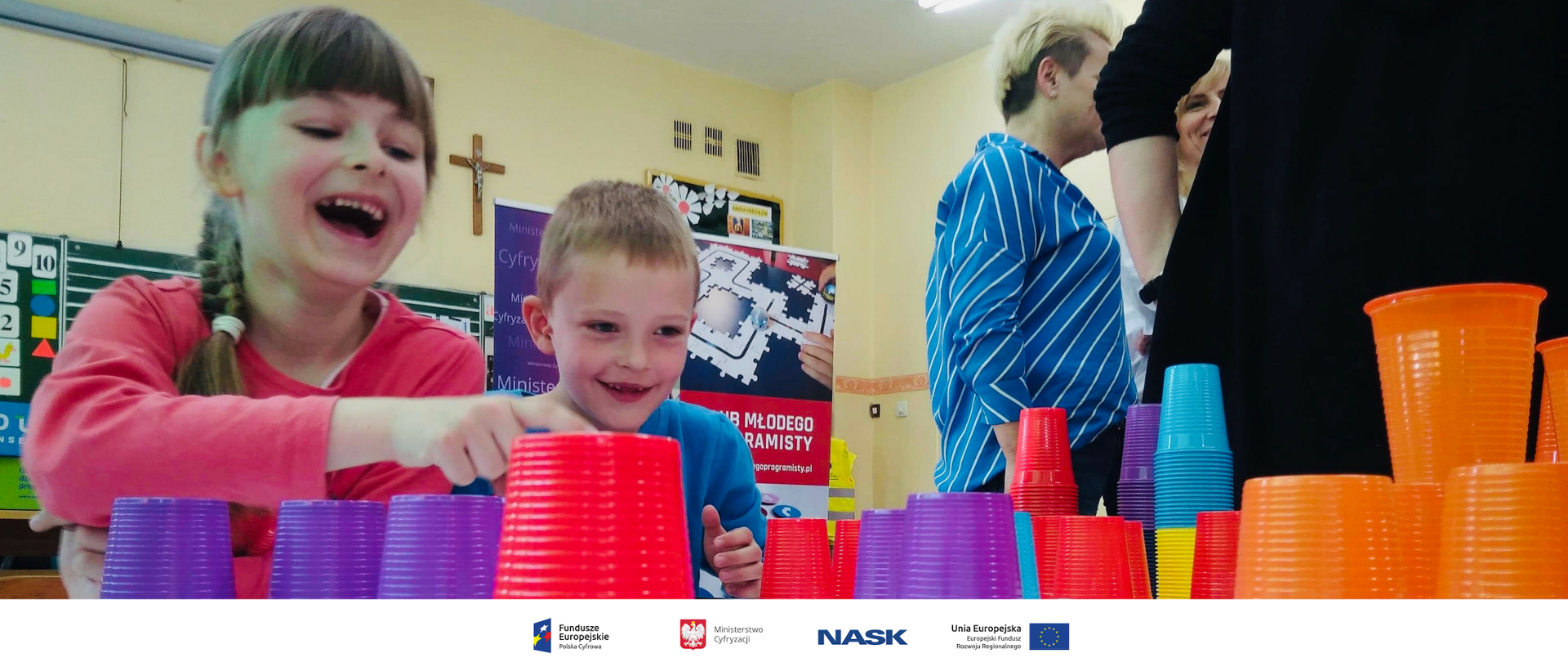 Na zdjęciu widzmy dwójkę dzieci bawiącą się kolorowymi kubkami.