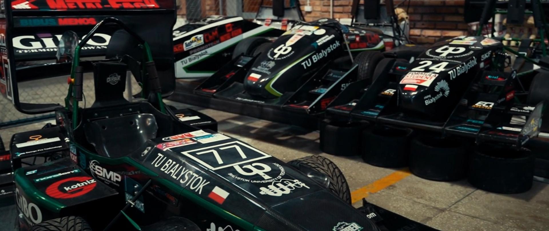 Zdjęcie pojazdu - bolidu wyścigowego, podłużny ciemnozielony pojazd z dużymi spojlerami i napisem 77 TU Białystok.